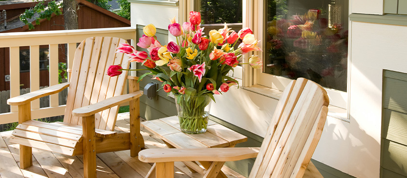 2 chairs on porch next to small table with flowers on it
